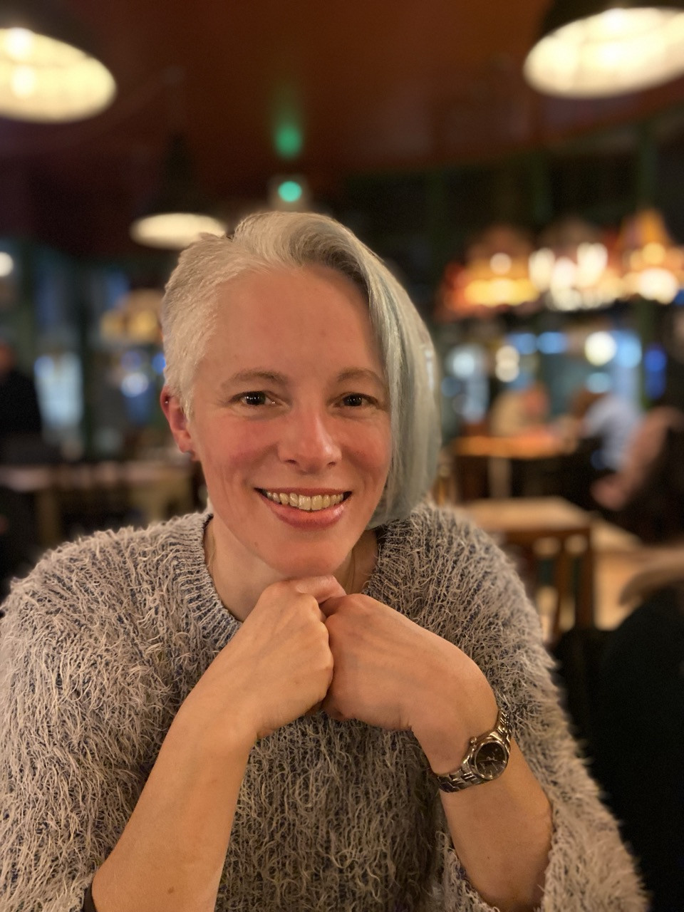 Diny smiling at a table, resting her chin on her hands