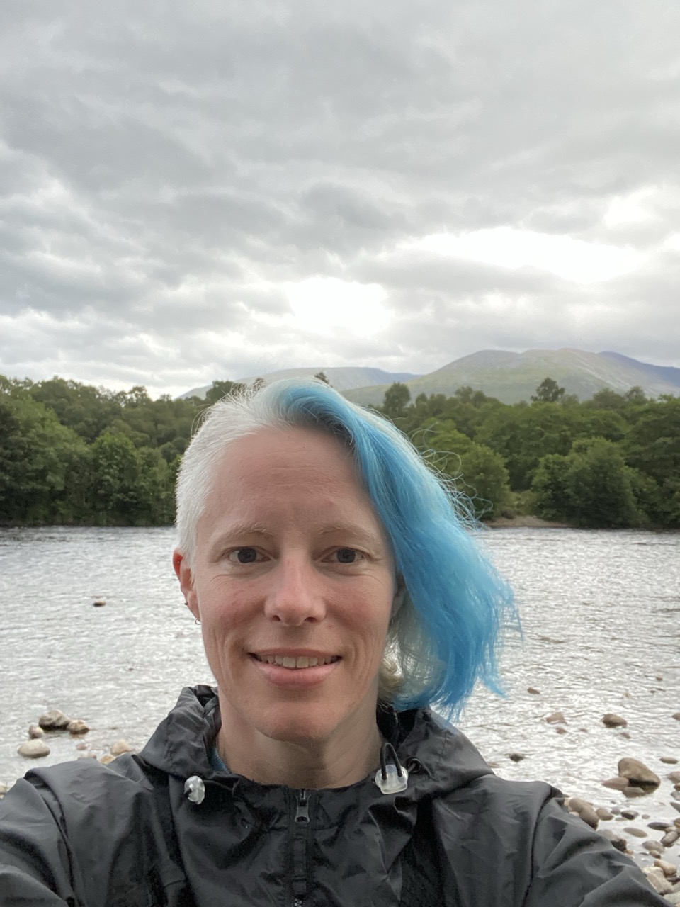 Diny beside a lake and mountains, with her electric-blue hair