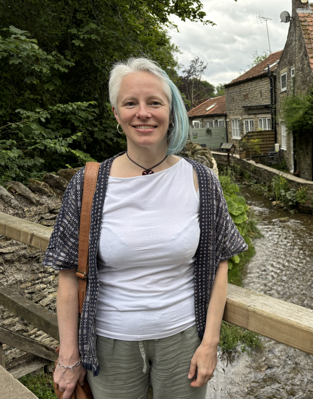Diny smiling beside a village stream and stone cottages